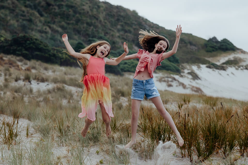 Tween girls jumping at Ocean Beach Whangarei during a family portrait session.