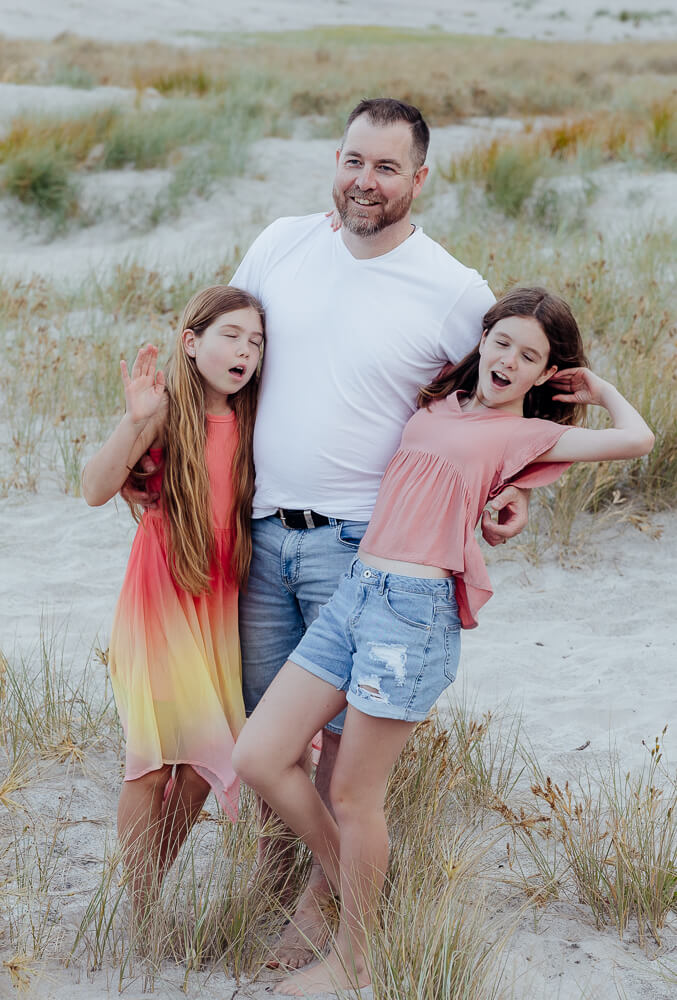 Tween girls laughing with their Dad at Ocean Beach Whangarei during a family portrait session.